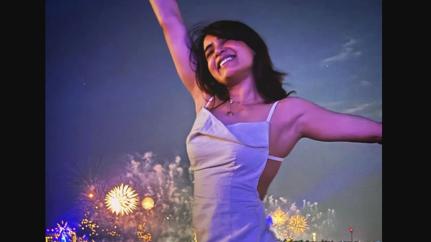 In another post, Samantha shared her picture posing candidly for the lens, spreading her arms, fireworks in the backdrop. She is wearing a white thigh-high slit dress with thin straps